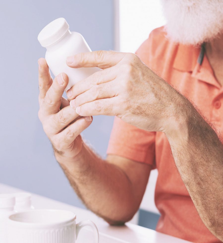 An older man checking the label on a prescription bottle at his kitchen counter